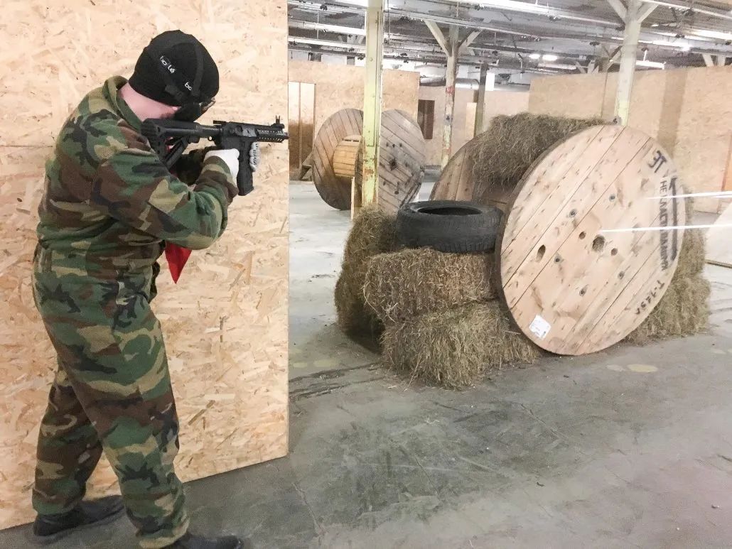 Airsofta spēlētājs tēmē aiz koka spoles iekštelpu laukumā