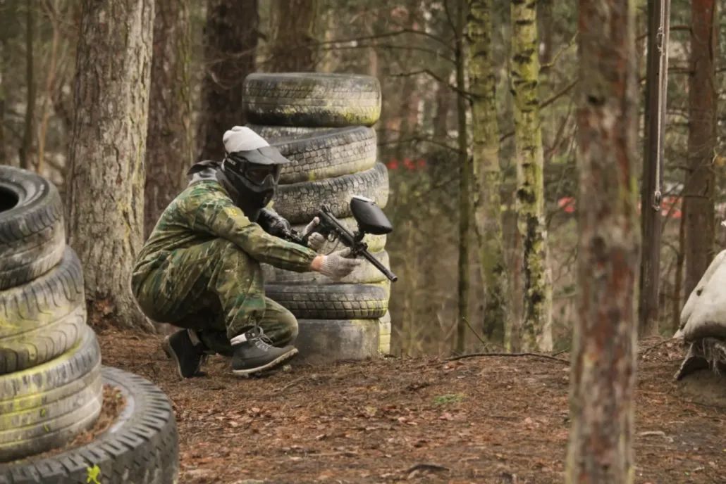 Peintbola spēlētājs maskā aiz riepu aizsega meža laukumā