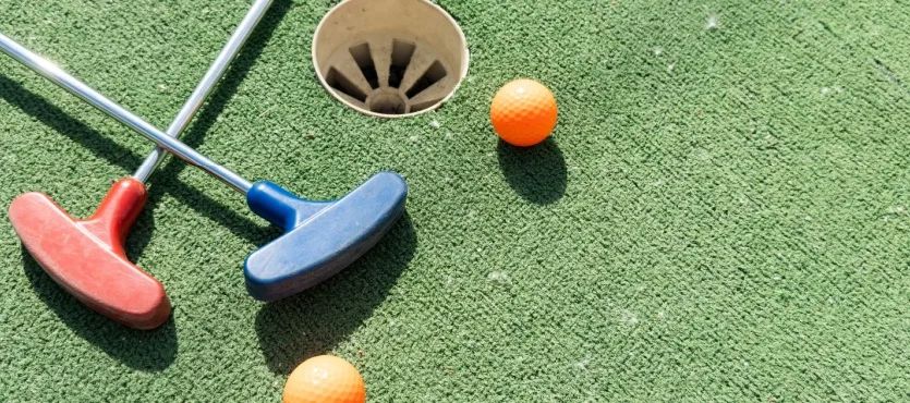 Two putters and orange balls beside a mini golf hole