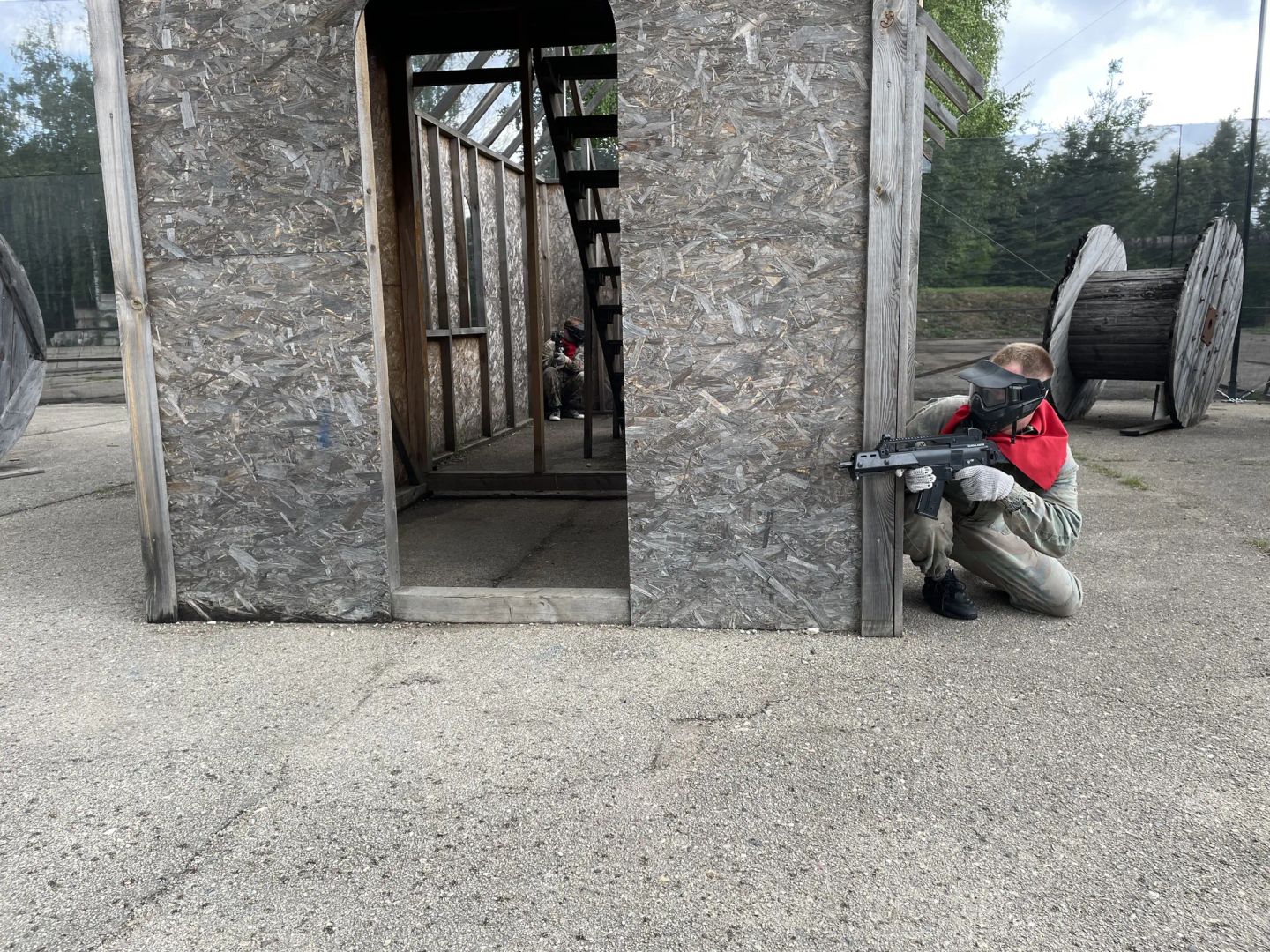 Airsofta spēlētājs aiz koka sienas Šampētera āra laukumā